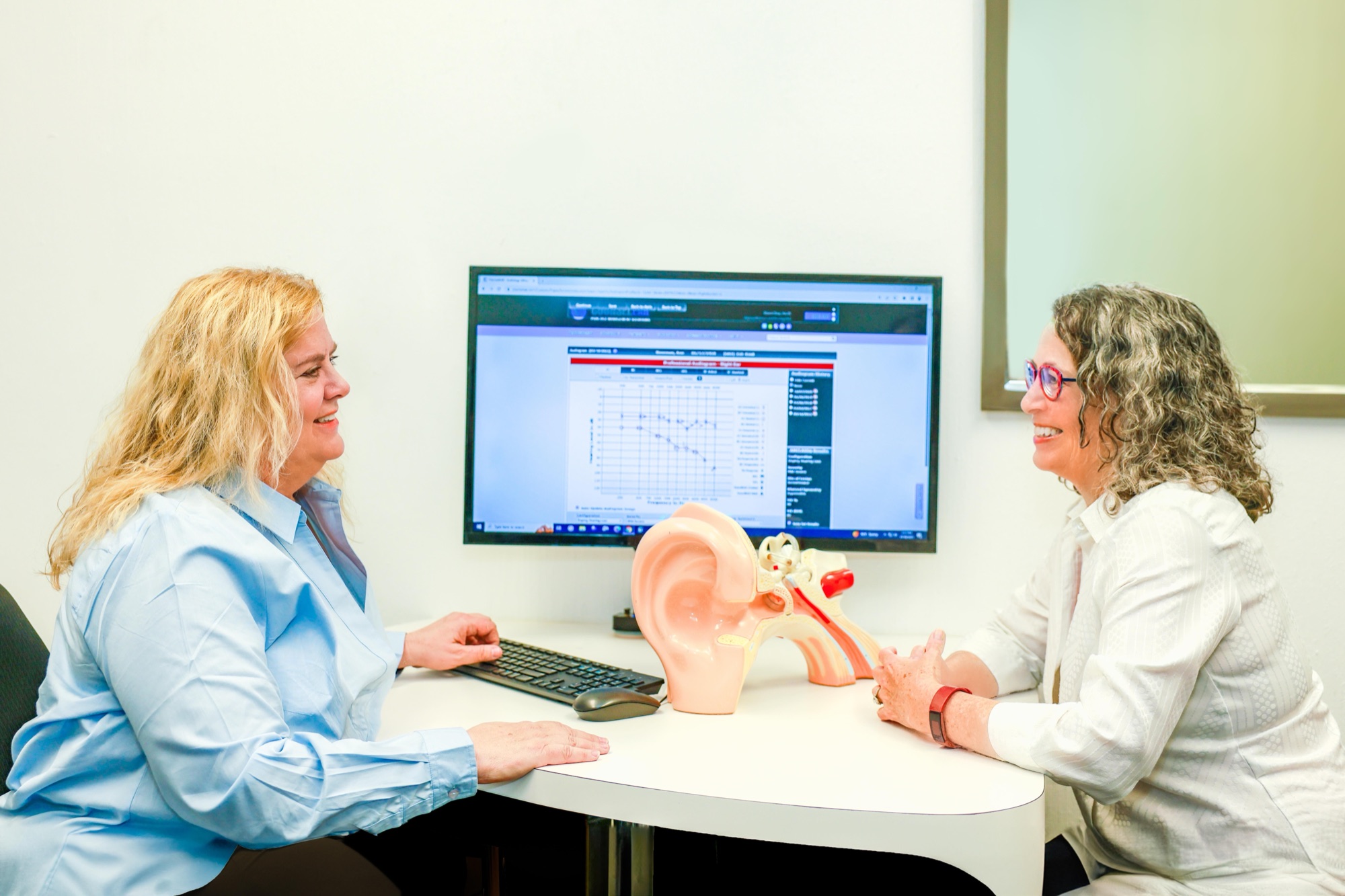 Dr. Day at her desk, smiling, with hearing test results on the screen